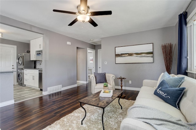 living room featuring ceiling fan, stacked washer / dryer, and dark hardwood / wood-style floors