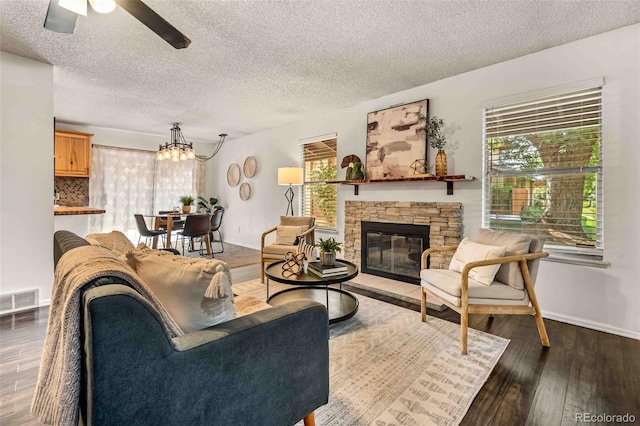 living room with dark wood-type flooring, ceiling fan with notable chandelier, a textured ceiling, and a stone fireplace