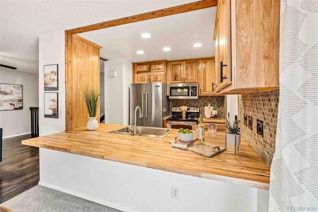 kitchen with stainless steel appliances, sink, kitchen peninsula, wooden counters, and dark wood-type flooring