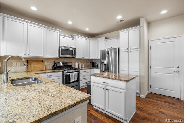 kitchen featuring stainless steel appliances, a sink, white cabinets, light stone counters, and dark wood-type flooring