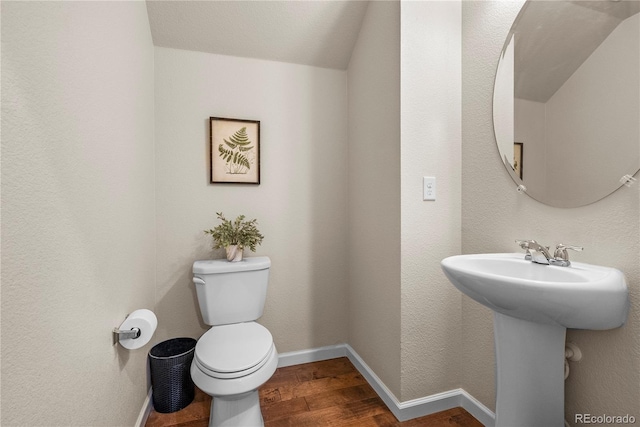 half bathroom featuring wood finished floors, toilet, baseboards, and a sink