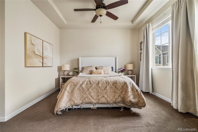 bedroom featuring a raised ceiling, dark colored carpet, and baseboards