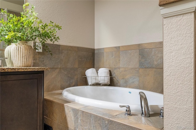 bathroom with a garden tub, vanity, and a textured wall