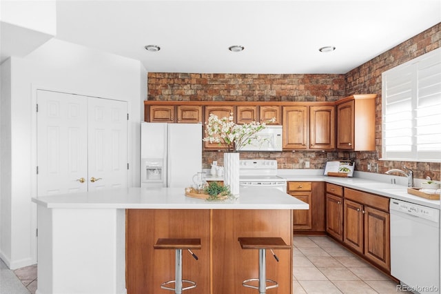 kitchen featuring a sink, white appliances, brown cabinetry, light countertops, and a kitchen island