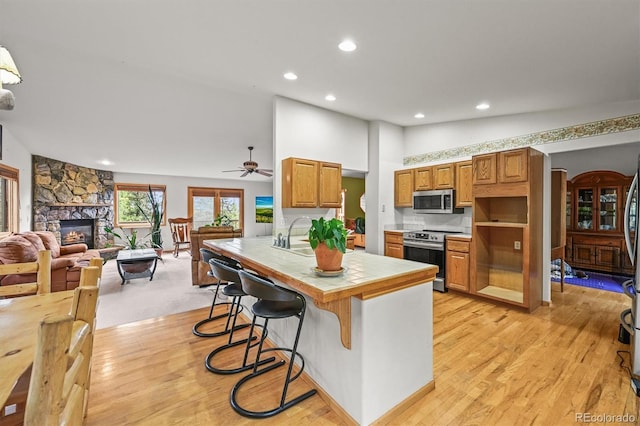 29825 Kennedy Gulch Rd, Conifer, CO 80433 - kitchen featuring appliances with stainless steel finishes, tile counters, a stone fireplace, recessed lighting, and light wood-style flooring