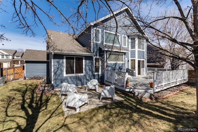 rear view of property featuring a lawn, a wooden deck, roof with shingles, and fence