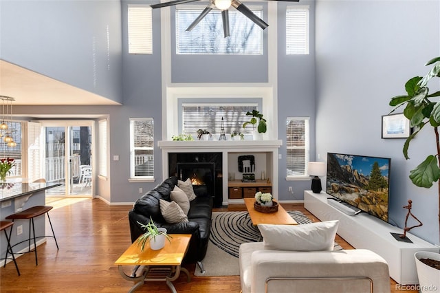 living area featuring a towering ceiling, wood finished floors, baseboards, and a high end fireplace