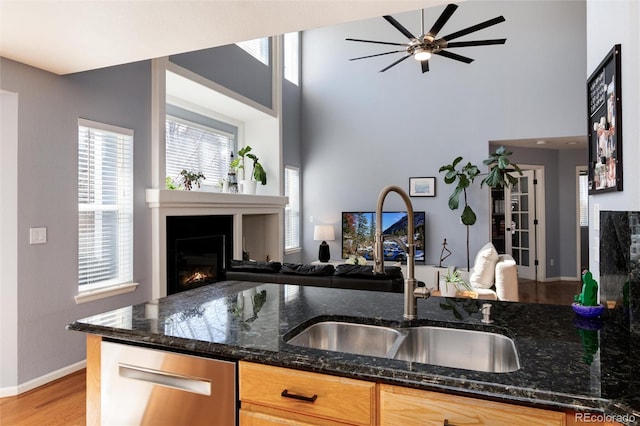 kitchen with a sink, wood finished floors, a glass covered fireplace, open floor plan, and dark stone counters