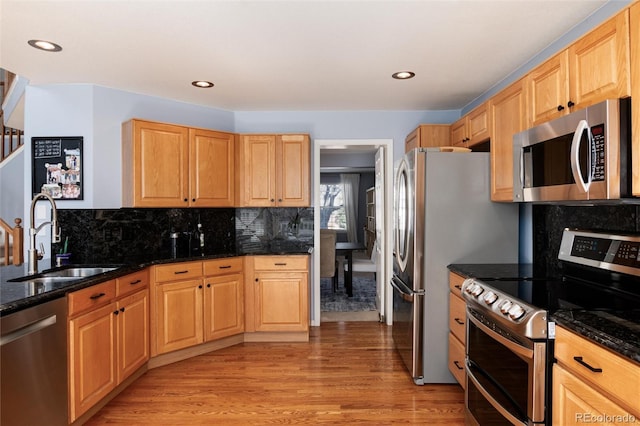 kitchen featuring dark stone counters, light wood-type flooring, appliances with stainless steel finishes, and a sink