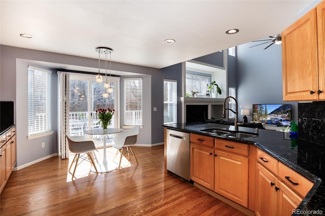 kitchen with a peninsula, a sink, hanging light fixtures, dishwasher, and light wood-type flooring