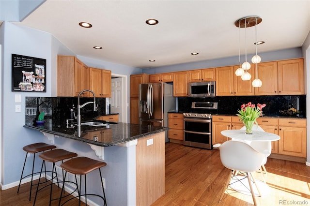 kitchen with a kitchen bar, a sink, appliances with stainless steel finishes, a peninsula, and light wood finished floors