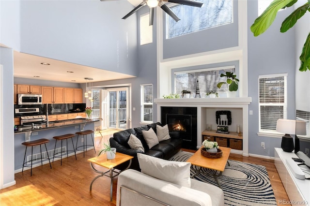 living room with baseboards, light wood-style floors, a ceiling fan, and a tile fireplace