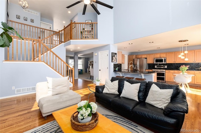 living room featuring visible vents, light wood finished floors, a ceiling fan, and stairway