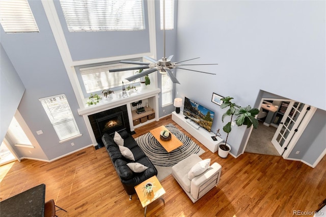 living area featuring baseboards, wood finished floors, a towering ceiling, and a tile fireplace