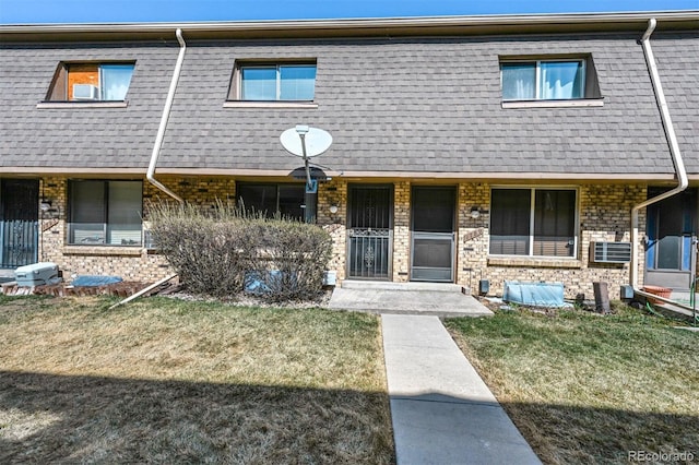 townhome / multi-family property with mansard roof, brick siding, a front yard, and a shingled roof