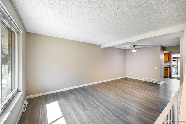 unfurnished living room with a textured ceiling, wood finished floors, visible vents, and baseboards