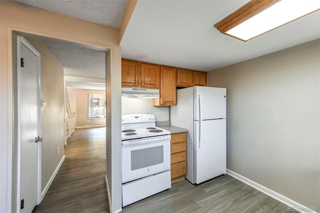 kitchen featuring under cabinet range hood, white appliances, dark wood-type flooring, and baseboards