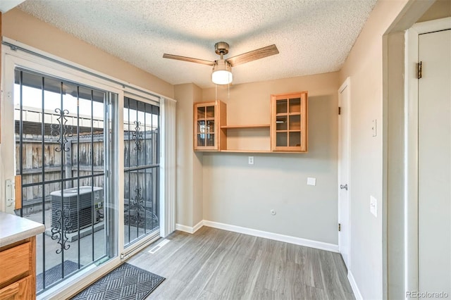 interior space with baseboards, a textured ceiling, wood finished floors, and a ceiling fan