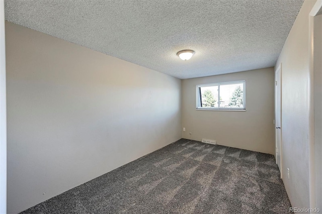 empty room with visible vents, dark colored carpet, and a textured ceiling