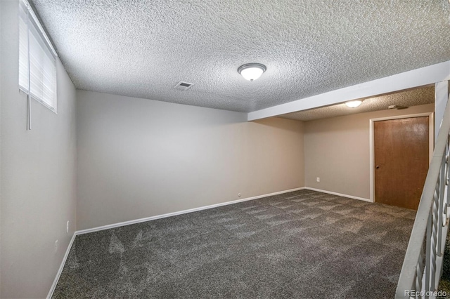 spare room featuring a textured ceiling, visible vents, dark colored carpet, and baseboards