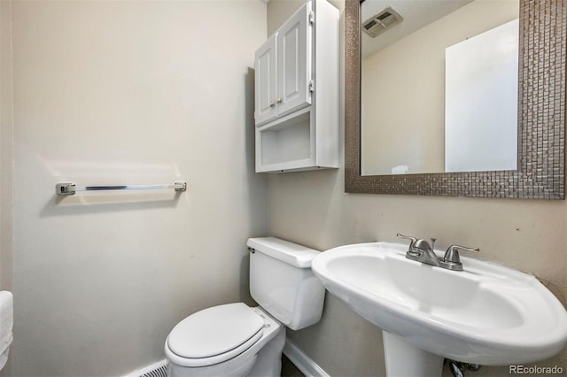 half bathroom featuring visible vents, toilet, baseboards, and a sink