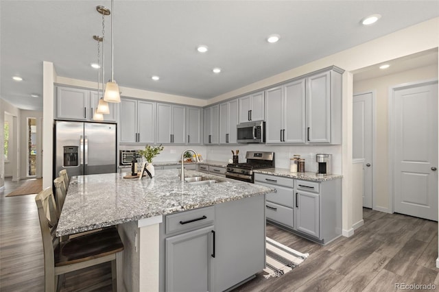 1061 S De Gaulle Ct, Aurora, CO 80018 - kitchen with appliances with stainless steel finishes, gray cabinetry, a breakfast bar, light stone counters, and wood finished floors