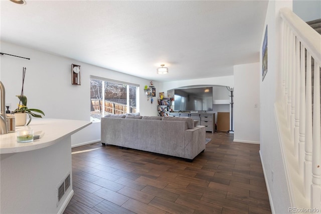 living room with arched walkways, dark wood-type flooring, visible vents, and baseboards