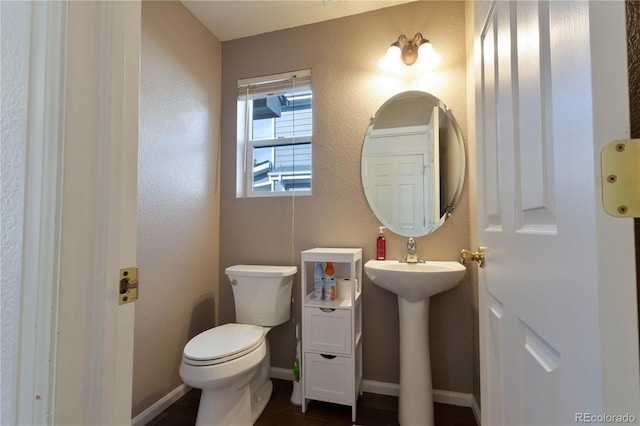 bathroom with toilet, baseboards, a sink, and a textured wall