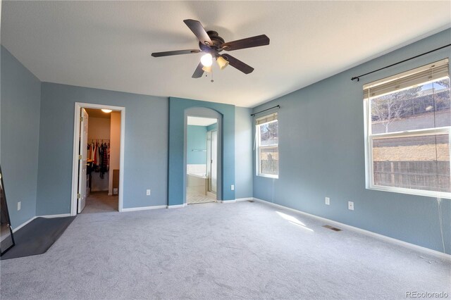 unfurnished bedroom featuring carpet floors, a walk in closet, a ceiling fan, ensuite bath, and baseboards