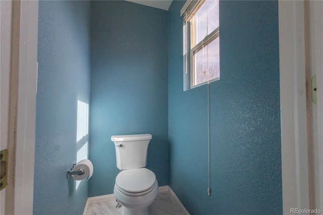 bathroom featuring toilet, marble finish floor, and baseboards