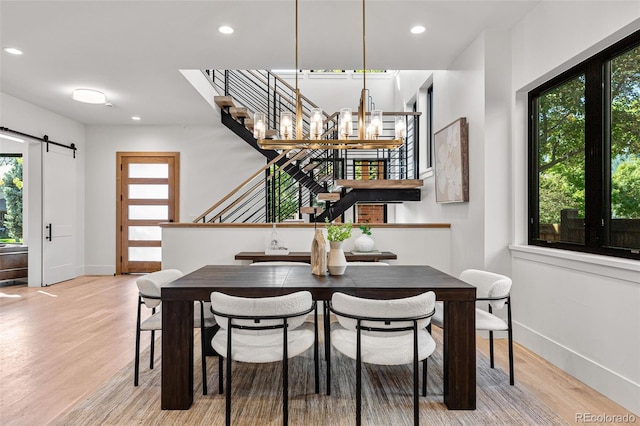 dining space with a notable chandelier, light wood-type flooring, and a barn door