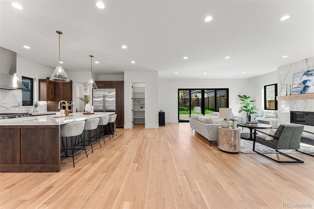 kitchen with stainless steel built in fridge, a breakfast bar area, light hardwood / wood-style flooring, and dark brown cabinetry