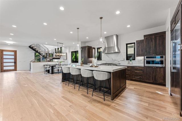 kitchen featuring light hardwood / wood-style flooring, appliances with stainless steel finishes, a kitchen island, and wall chimney range hood