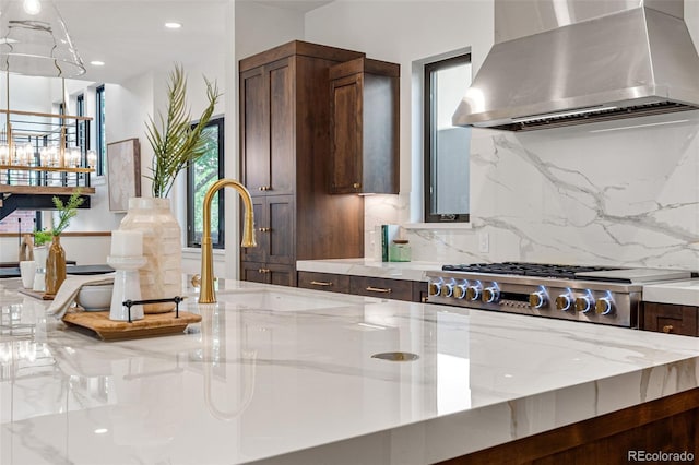 kitchen with light stone countertops, decorative backsplash, wall chimney range hood, and sink