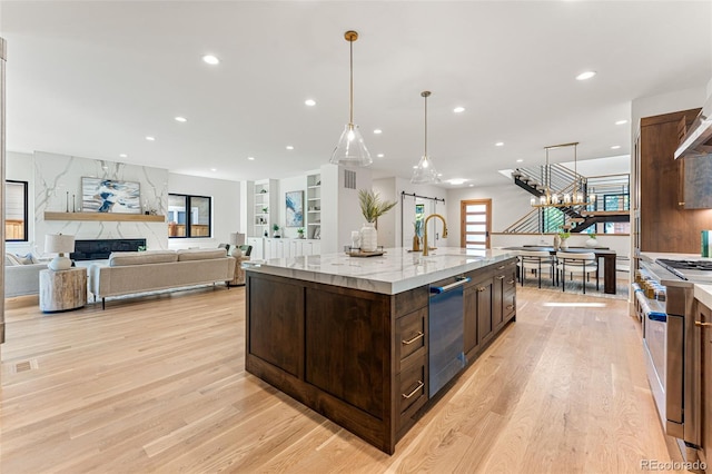 kitchen featuring an island with sink, light hardwood / wood-style floors, dark brown cabinets, an inviting chandelier, and a barn door