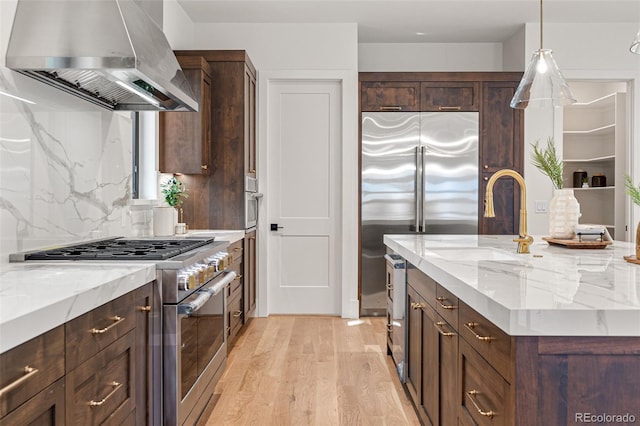 kitchen featuring light stone countertops, wall chimney exhaust hood, light wood-type flooring, and high end appliances