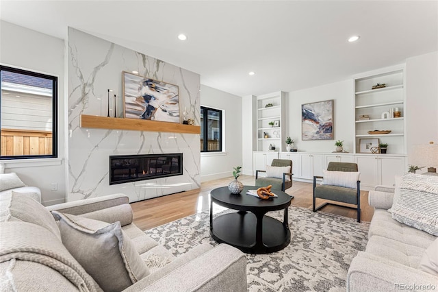 living room featuring light hardwood / wood-style flooring, a high end fireplace, and built in features