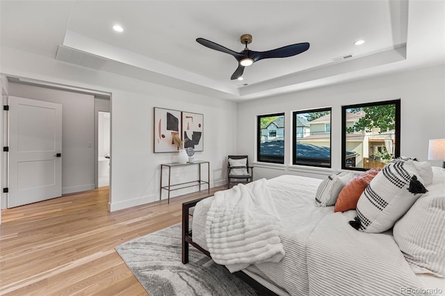 bedroom featuring ceiling fan, light hardwood / wood-style flooring, and a raised ceiling