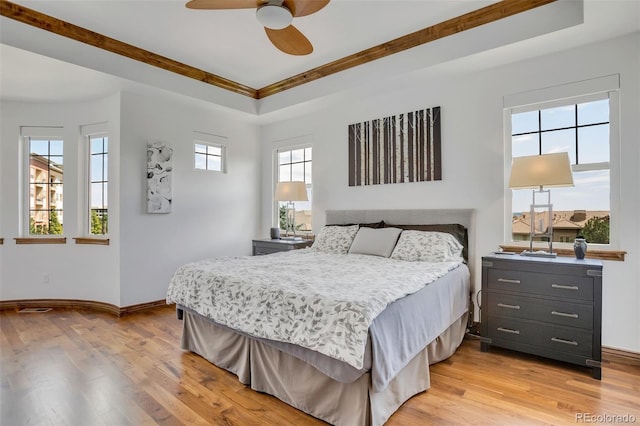 bedroom with a raised ceiling, ceiling fan, and light wood-type flooring