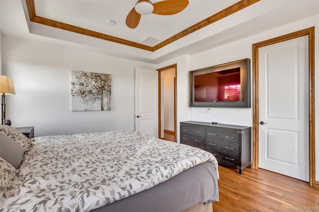 bedroom with light hardwood / wood-style floors, ceiling fan, a tray ceiling, and crown molding