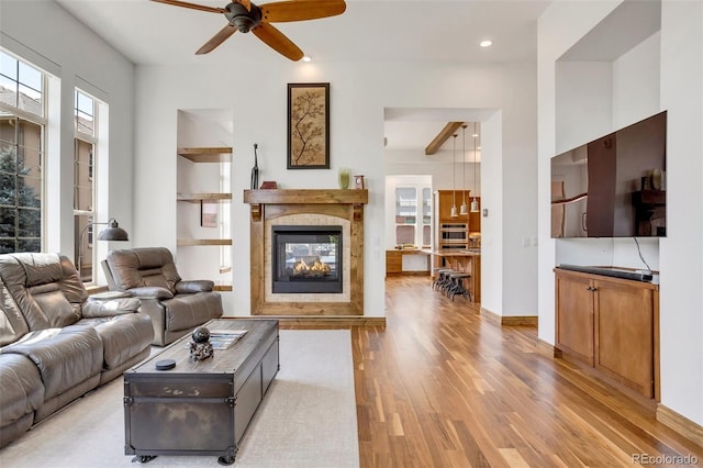 living room featuring light hardwood / wood-style floors, ceiling fan, a multi sided fireplace, and beam ceiling