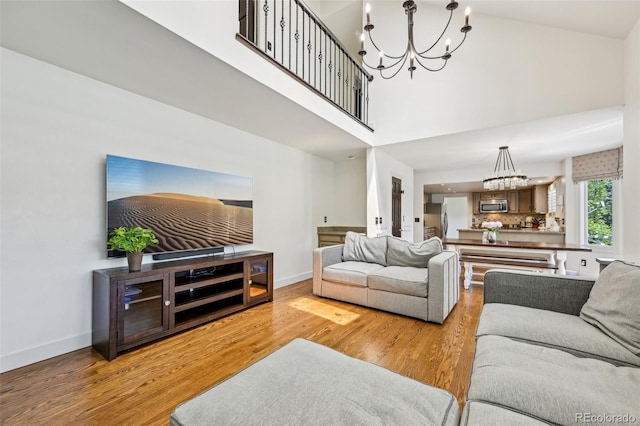 living room with a chandelier, wood finished floors, baseboards, and a high ceiling