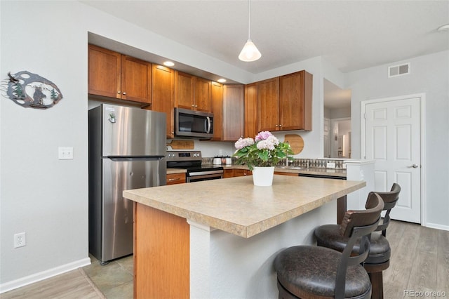 kitchen with visible vents, a breakfast bar, light countertops, brown cabinets, and appliances with stainless steel finishes