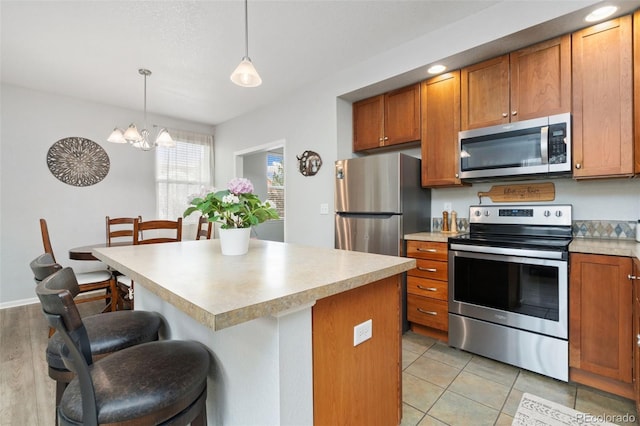 kitchen featuring brown cabinetry, an inviting chandelier, light countertops, appliances with stainless steel finishes, and a kitchen bar