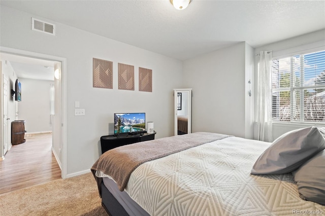 bedroom featuring visible vents, light colored carpet, a textured ceiling, and baseboards