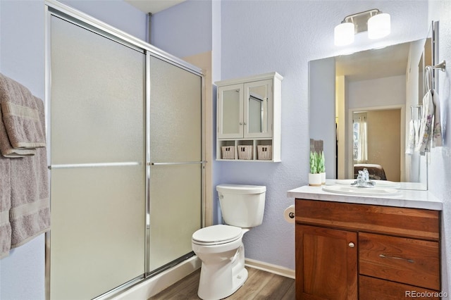 bathroom featuring a shower stall, baseboards, toilet, wood finished floors, and vanity