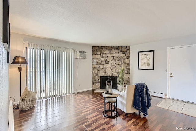 living room with a textured ceiling, a wall mounted AC, baseboard heating, hardwood / wood-style floors, and a stone fireplace