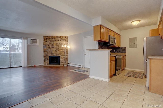 kitchen with a baseboard radiator, tasteful backsplash, a stone fireplace, a wall unit AC, and stove