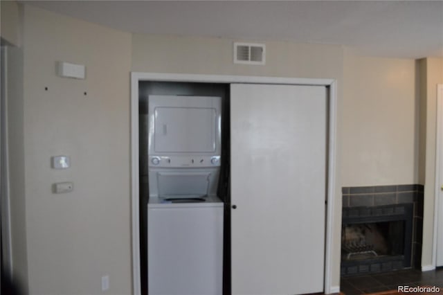 washroom with a tile fireplace, stacked washing maching and dryer, and dark wood-type flooring