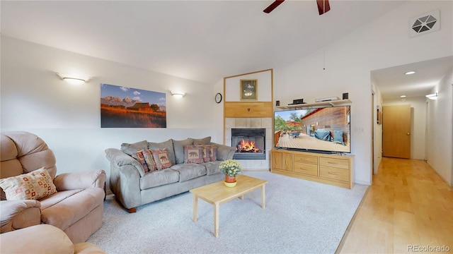 living room featuring light wood-type flooring, a tiled fireplace, ceiling fan, and vaulted ceiling